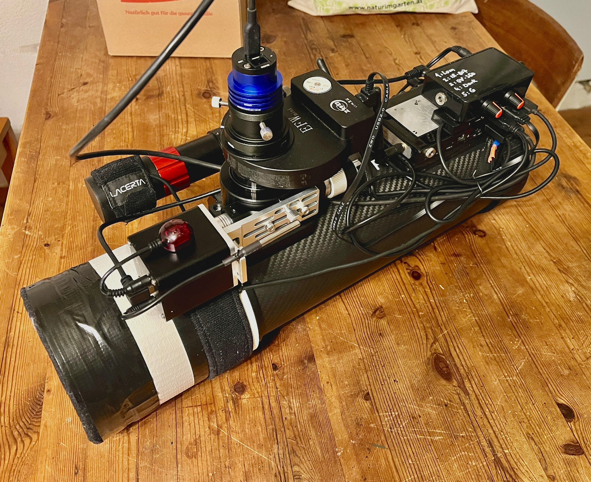 IMG_0213 Für experimentelle Aufnahmen habe ich diesen kleinen Newton zusammengestellt: TS Photon 4,5" f4 mit 458mm Brennweite. Die Kamera wurde speziell für diesen Zweck ausgewählt, eine QHY 5 III 200M, deren Sensor hat mit 4µm zwar etwas zu große Pixel für das kleine Teleskop, aber ich habe sonst keinen halbwegs leistbaren Sensor gefunden, der sowohl in UV als auch in IR so eine hohe Effizienz bietet. Bei 350nm Wellenlänge (UV) hat dieser noch knapp 80% Quanteneffizienz. Alle Glaselemente wie Komakorrektor und Sensorfenster wurden entfernt, um die Transmission im UV-Bereich nicht weiter zu verringern. Dafür müssen die Sterne im Postprocessing korrigiert werden, was mit moderner Software kein Problem mehr ist. Über aktive Kühlung verfügt die Kamera nicht, es geht aber auch so. Um bequem die passenden Kalibrierungsaufnahmen zu jeder Session aufnehmen zu können, habe ich im Filterrad eine Position mit einer lichtundurchlässigen Scheibe belegt - so können Darkframes und BIAS Aufnahmen über die Steuerungssoftware programmiert werden ohne dass ich dafür extra aufstehen oder wach bleiben müsste. Die Steuerung übernimmt vorerst die kostenlose Software NINA, die auf dem Mini-PC installiert ist, den ich am hinteren Teleskopende befestigt habe. Gesteuert werden Hauptkamera, Filterrad, Fokusmotor und Guidekamera, sowie die Nachführung. Die beiden Tauheizungen sind manuell angesteuert über eine selbstgebaute Regeleinheit. Taukappe und rückseitiger Lichtschutz des Hauptspiegels sind mit einem 3D-Drucker in Eigenregie angefertigt. Das Teleskop selbst zeichnet sich nicht durch höchste Qualität der Komponenten aus, aber das muss es nicht, es ist ein Experimentierwerkzeug, das die eine oder andere Aufnahme in unsichtbaren Wellenlängen des Lichts ergänzen soll.